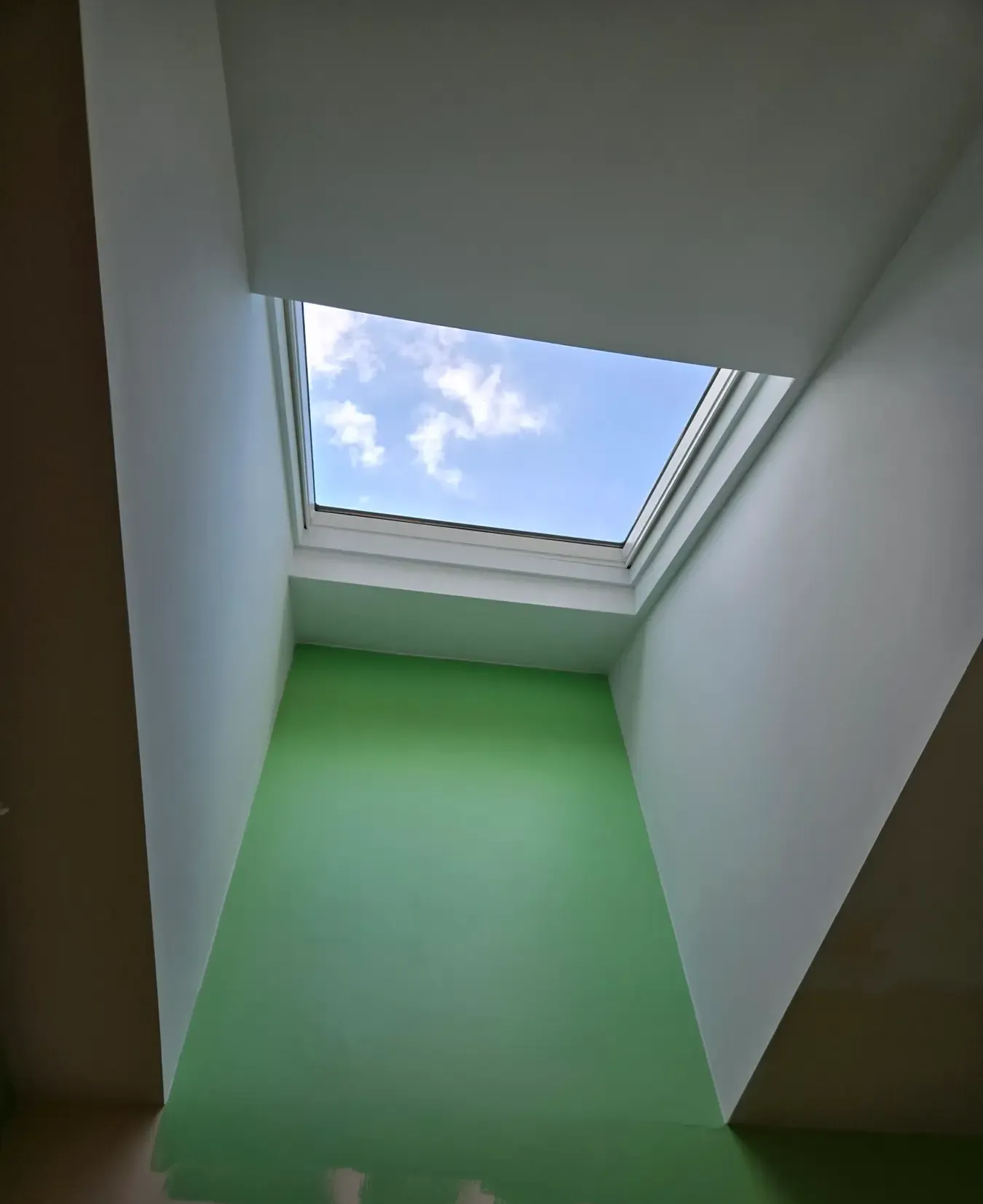 Skylight above a green interior wall, looking up at the ceiling opening to blue sky and clouds