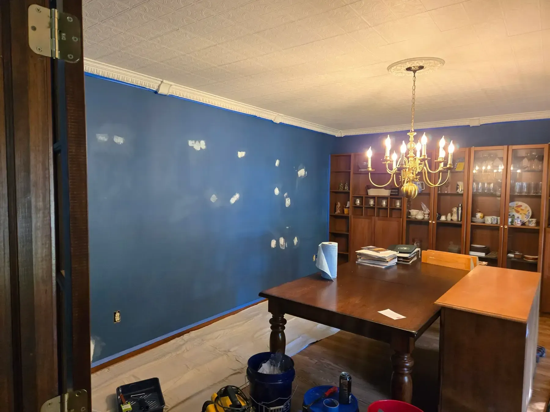 Dining room with blue walls, wooden table, chandelier, and china cabinet.