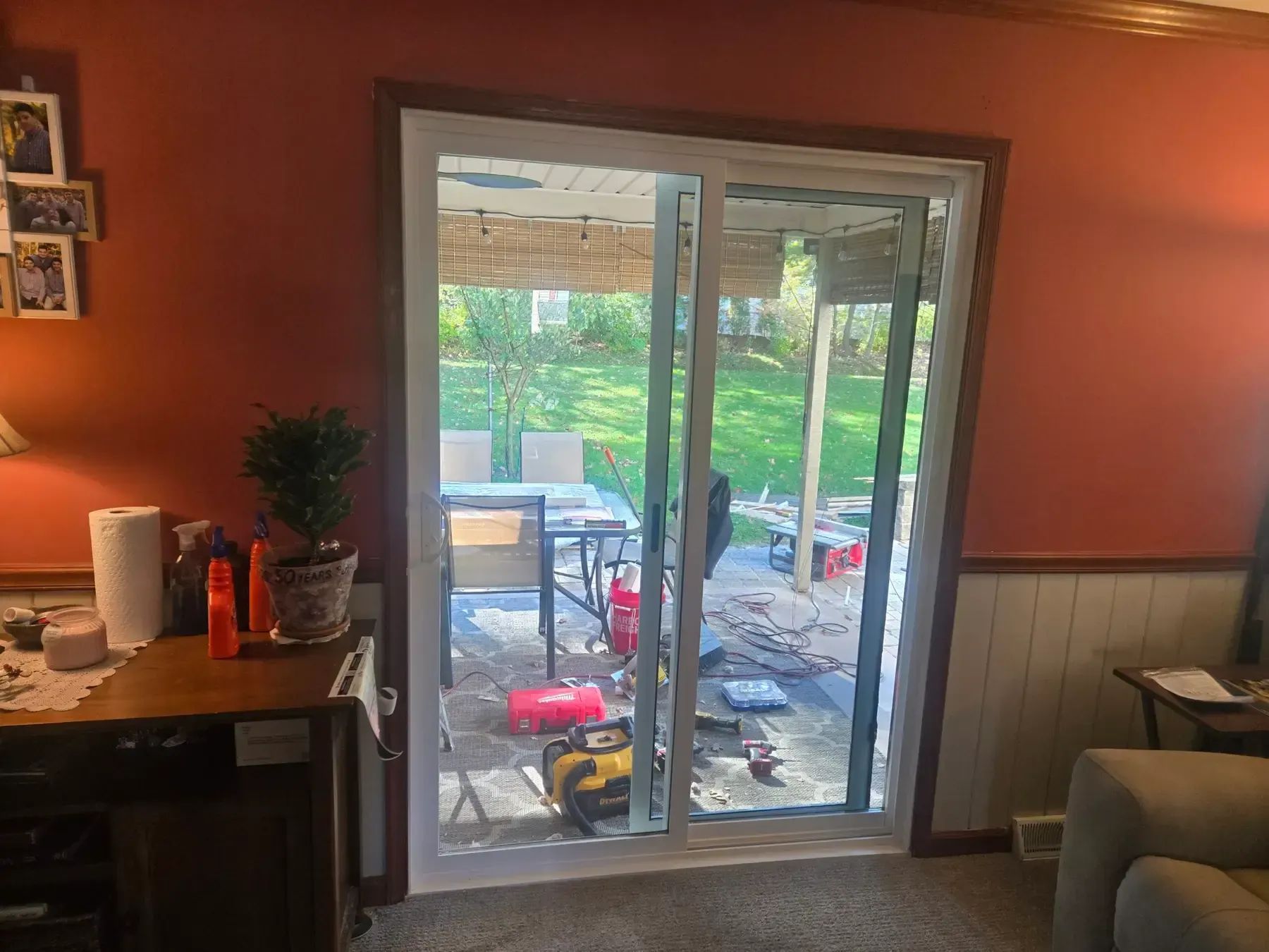 Living room with orange walls, sliding glass doors, and a patio view with outdoor tools and trees.