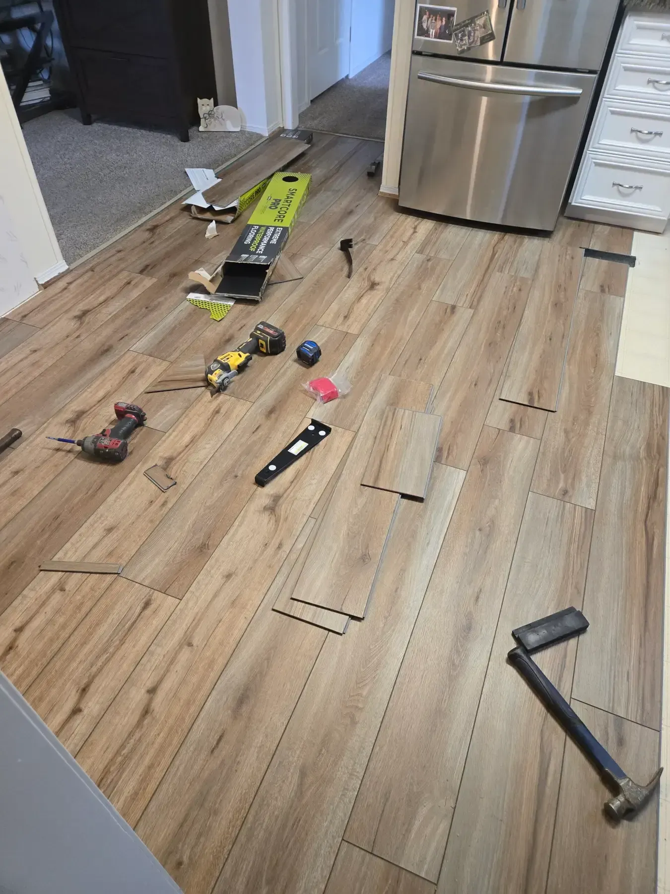 Toy tools scattered on a wood kitchen floor beside a stainless-steel refrigerator.