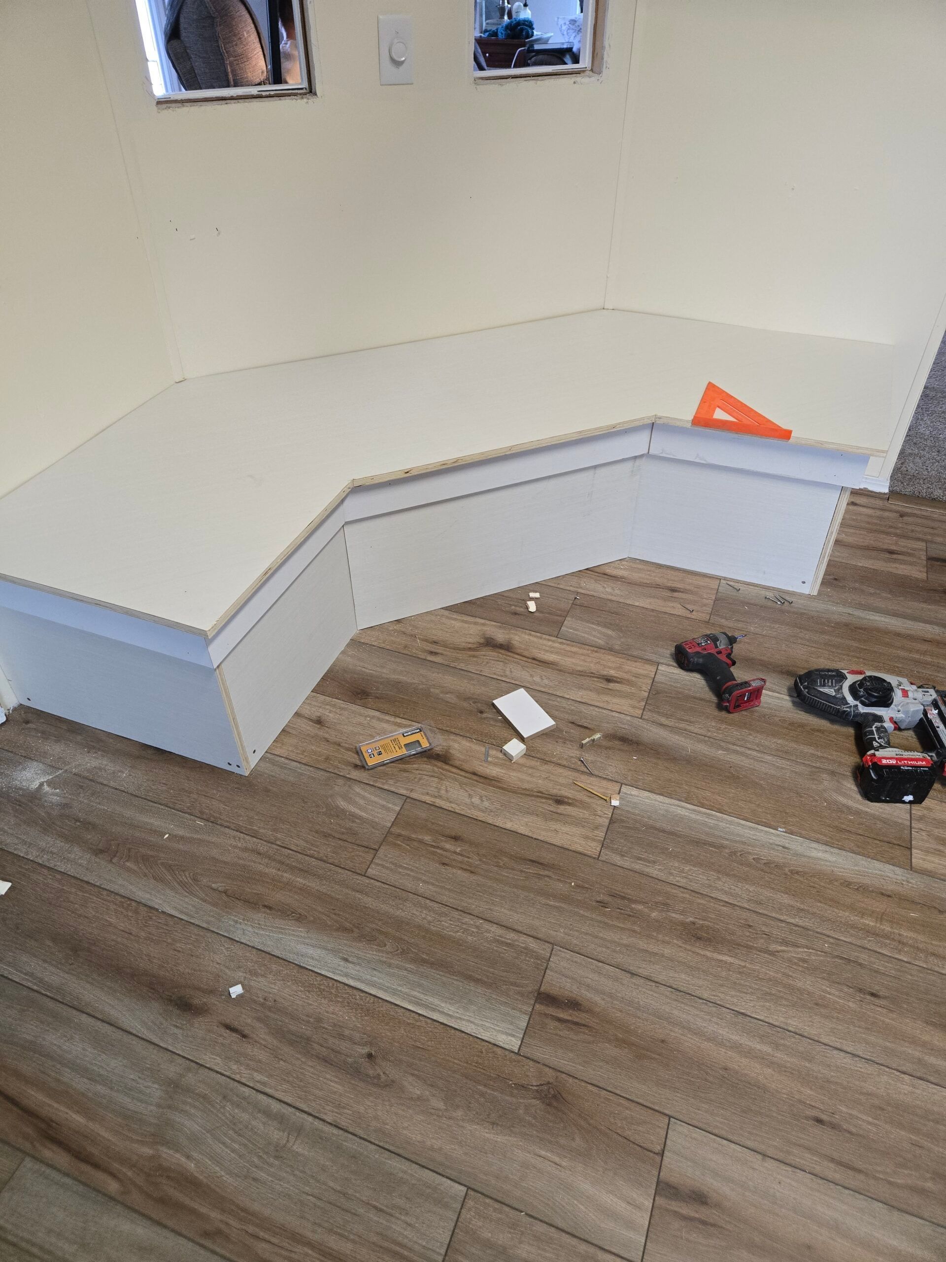 White L-shaped bench built along a wall in an unfinished room, with tools and materials on the floor.