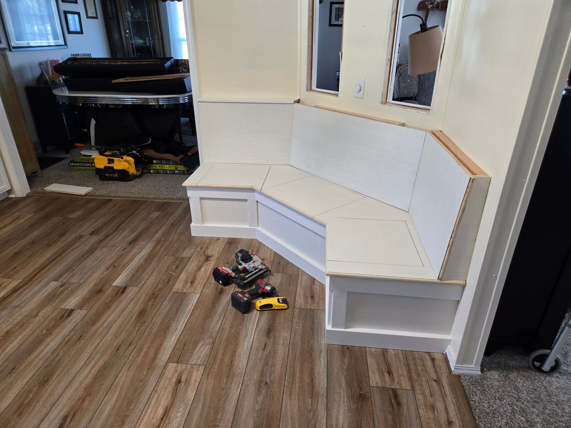 White built-in corner bench in a room with wood flooring; toy vehicles sit nearby.