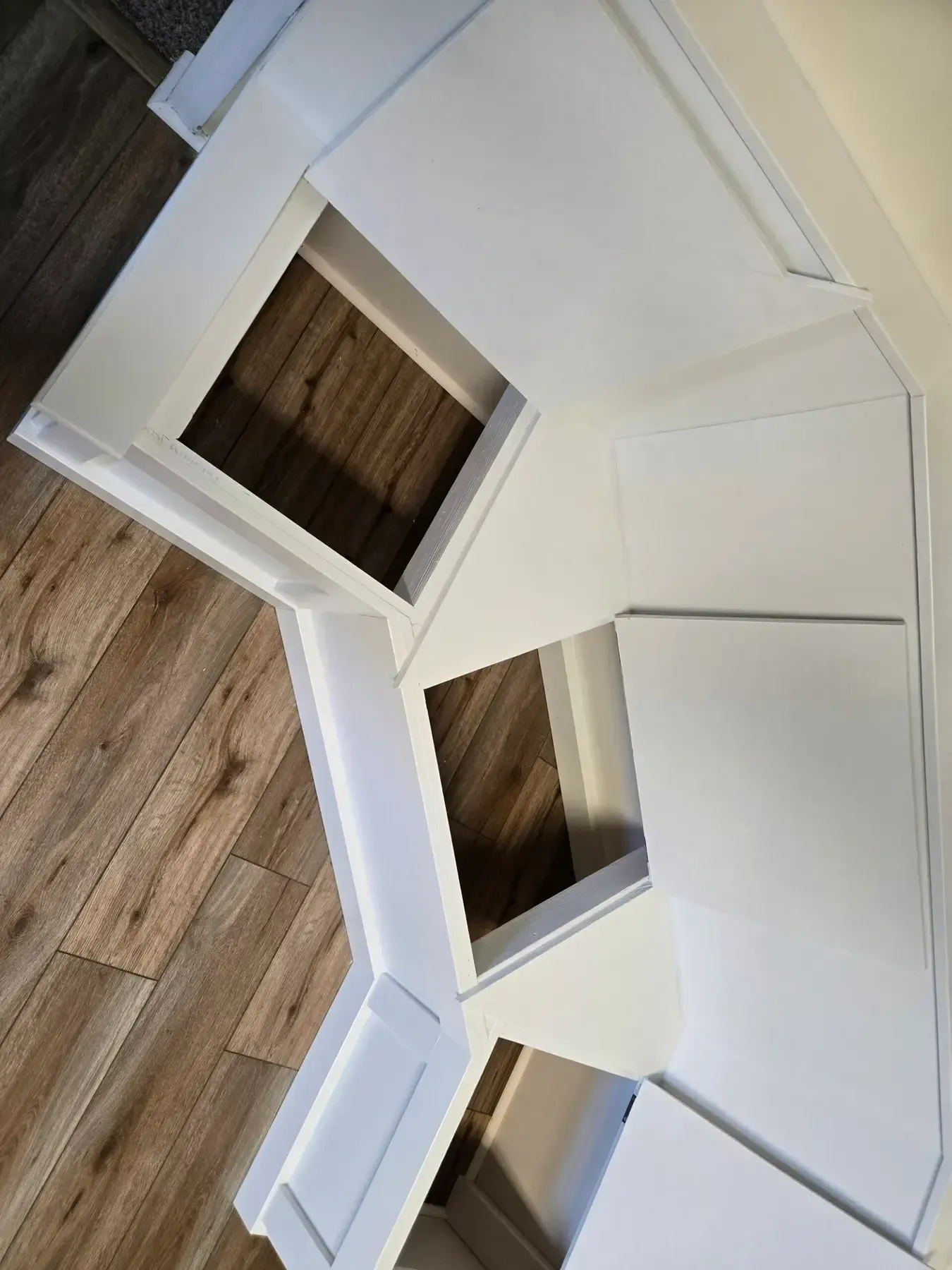 White geometric wooden shelf or wall unit on a wood floor, viewed at an angle.