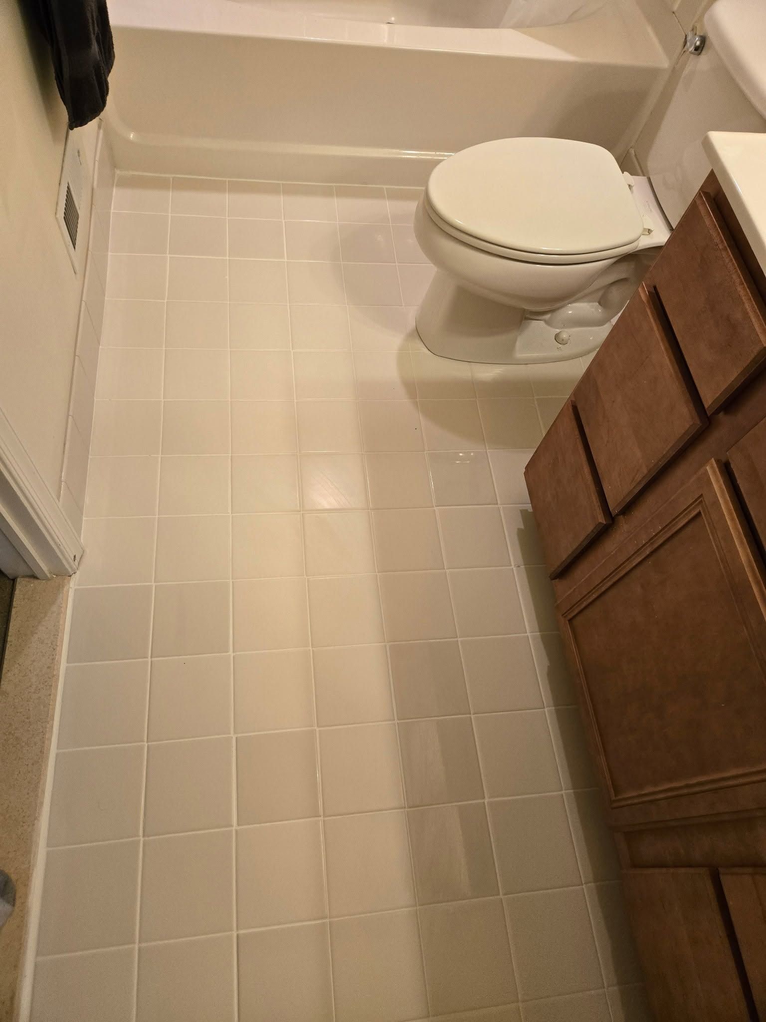 Small bathroom with white tile floor and a toilet beside a wooden vanity.