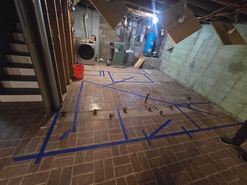 Tape-marked floor in an unfinished hallway with construction materials and tools.