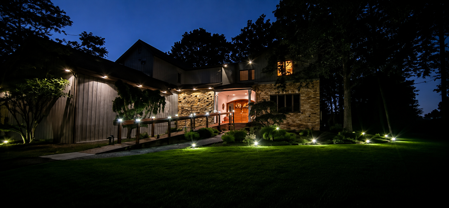 Nighttime view of a warmly lit stone house with a large lawn and trees silhouetted against the dark sky