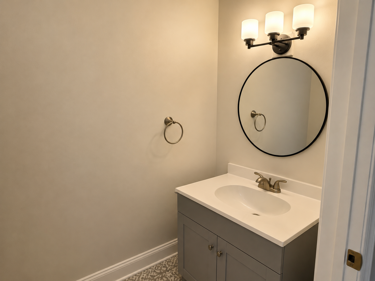 Small bathroom vanity with round mirror, wall sconce, and white sink against beige walls