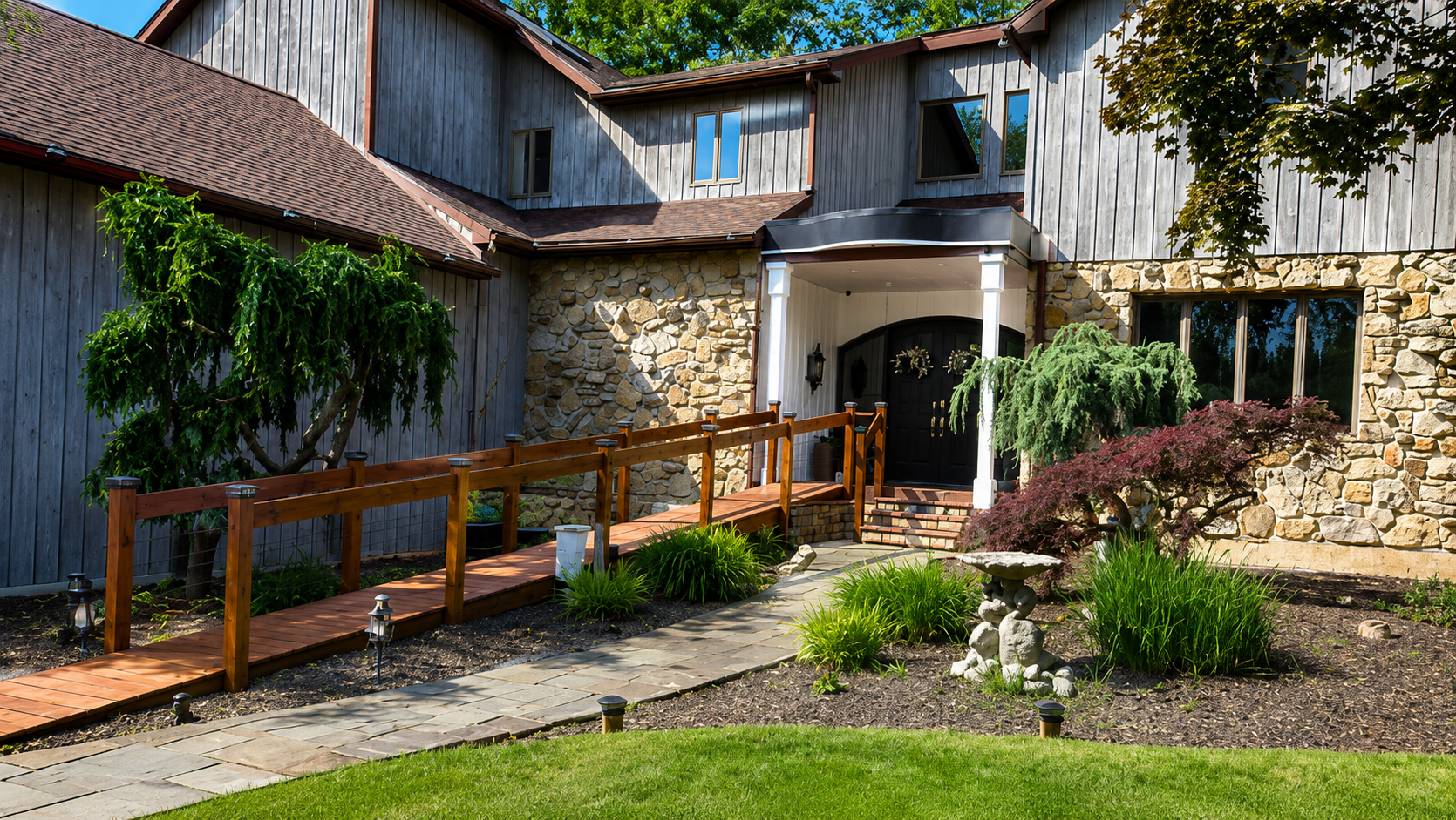 Courtyard with stone buildings, wooden walkway, flowers, and green lawn in bright sunlight