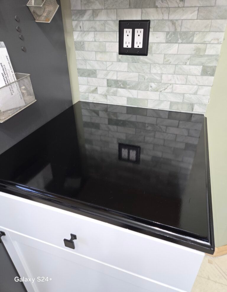 Black glass-top laundry sink with white cabinet and tiled backsplash in a kitchen or utility room
