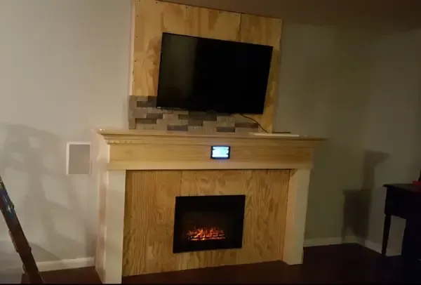 Living room fireplace with a TV above it, framed by light wood and stone, lit fire below.