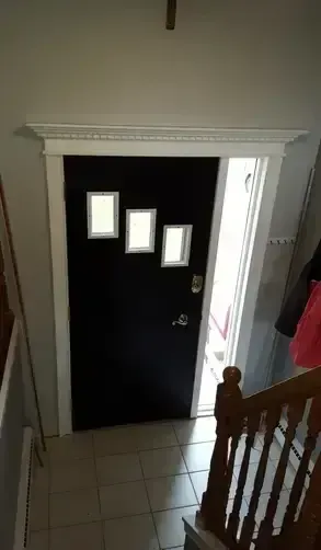 Stairwell landing with a black front door, three small windows, white trim, and tiled floor.