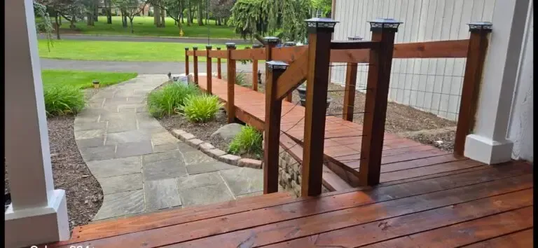Wooden porch and ramp with railing leading to a stone path in a green yard