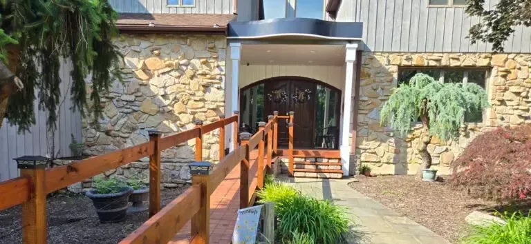 Wooden ramp leading to a stone building entrance with potted greenery and a small courtyard