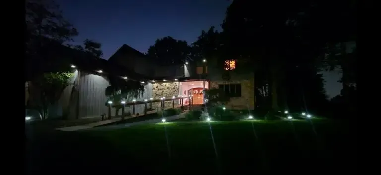 Nighttime view of a lit building and walkway beside a dark lawn with ground lights