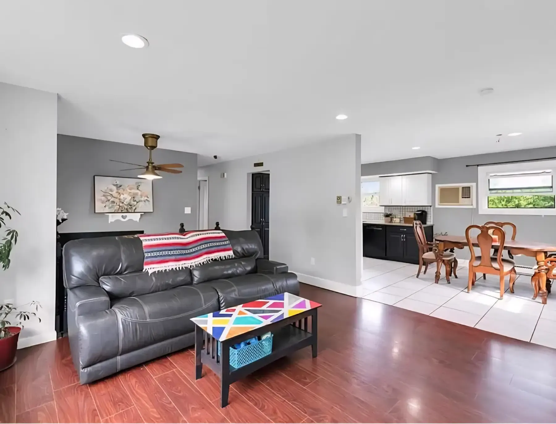 Bright living room with black sofa, colorful coffee table, and open dining area with wooden chairs
