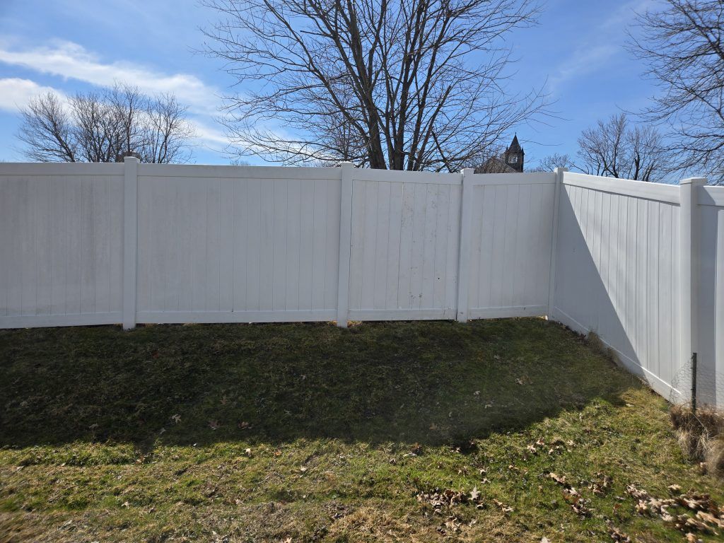 White vinyl fence along a grassy yard under a blue sky with bare trees behind it