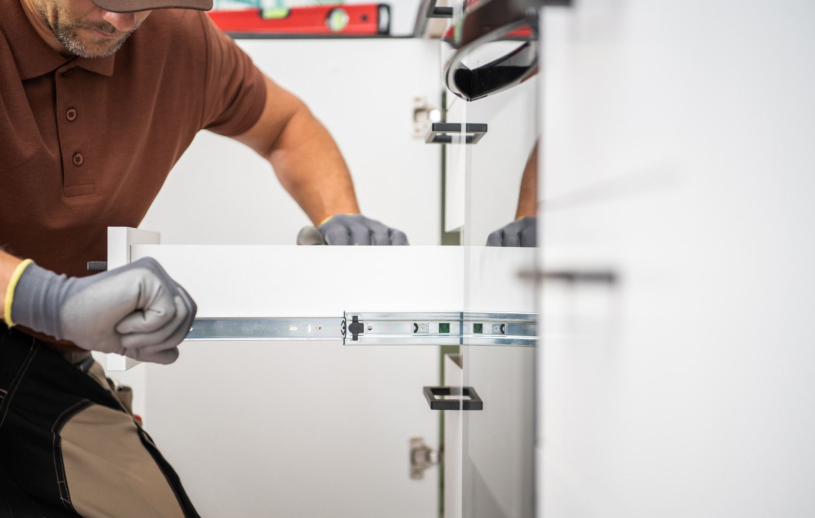 Technician adjusting a white cabinet hinge with a drill in a workshop-like setting