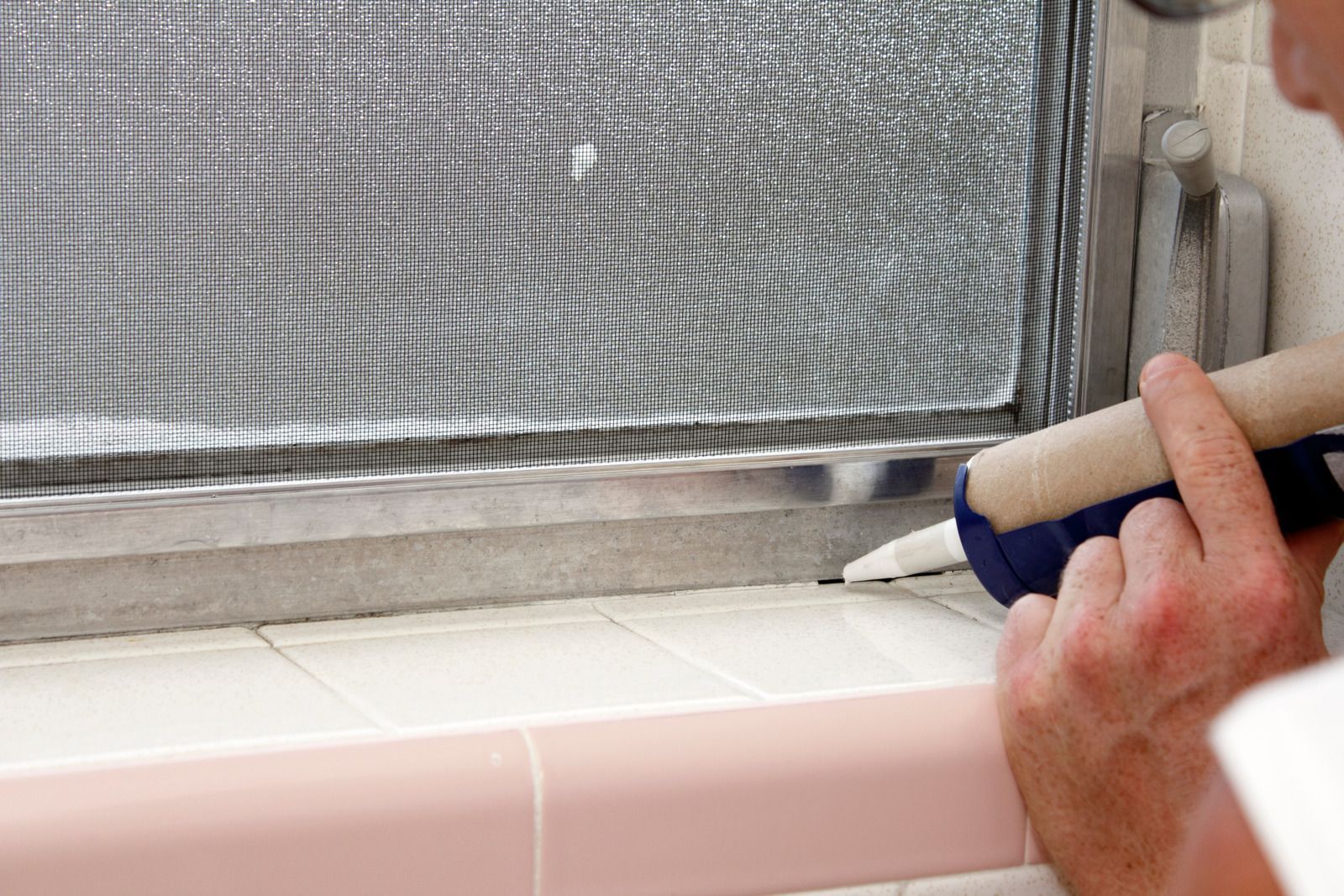 Hand caulking along a window frame with white sealant and a caulk gun