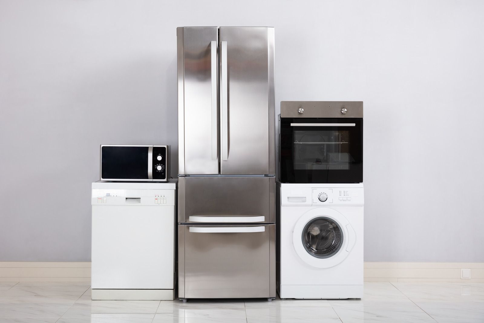 Modern kitchen appliances: microwave, refrigerator, oven, and washing machine on a white floor
