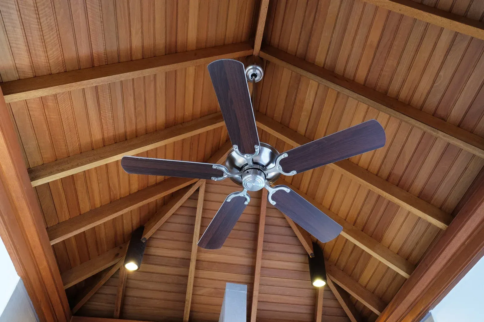 Ceiling fan with dark blades mounted on a wooden vaulted ceiling with exposed beams.
