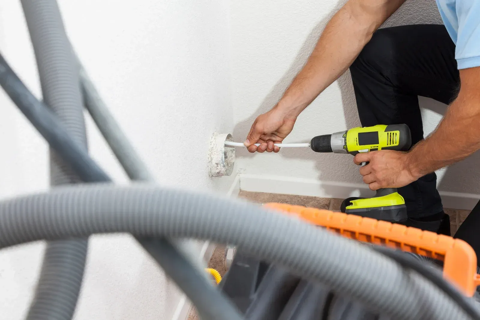 Person using a drill to install hardware on a white wall, with vacuum hoses in the foreground