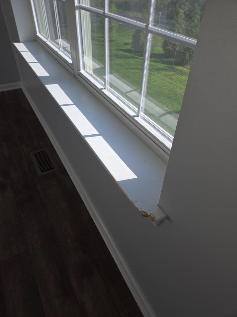 Sunlit window seat with white sill beside dark wood floor and a small chip in the paint