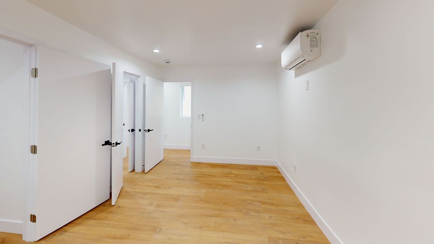 Empty room with white walls, light wood floor, and an air conditioning unit.