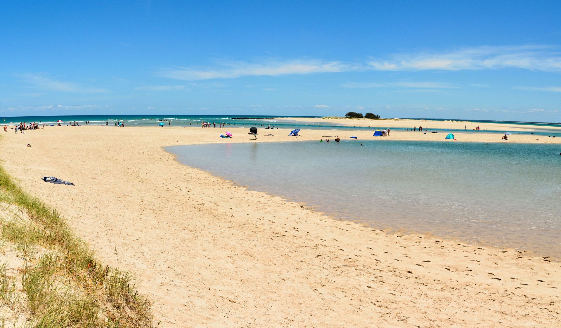 Sandy beach with calm water, people relaxing. Blue sky, distant islands. Sandy beach with calm water, people relaxing. Blue sky, distant islands.