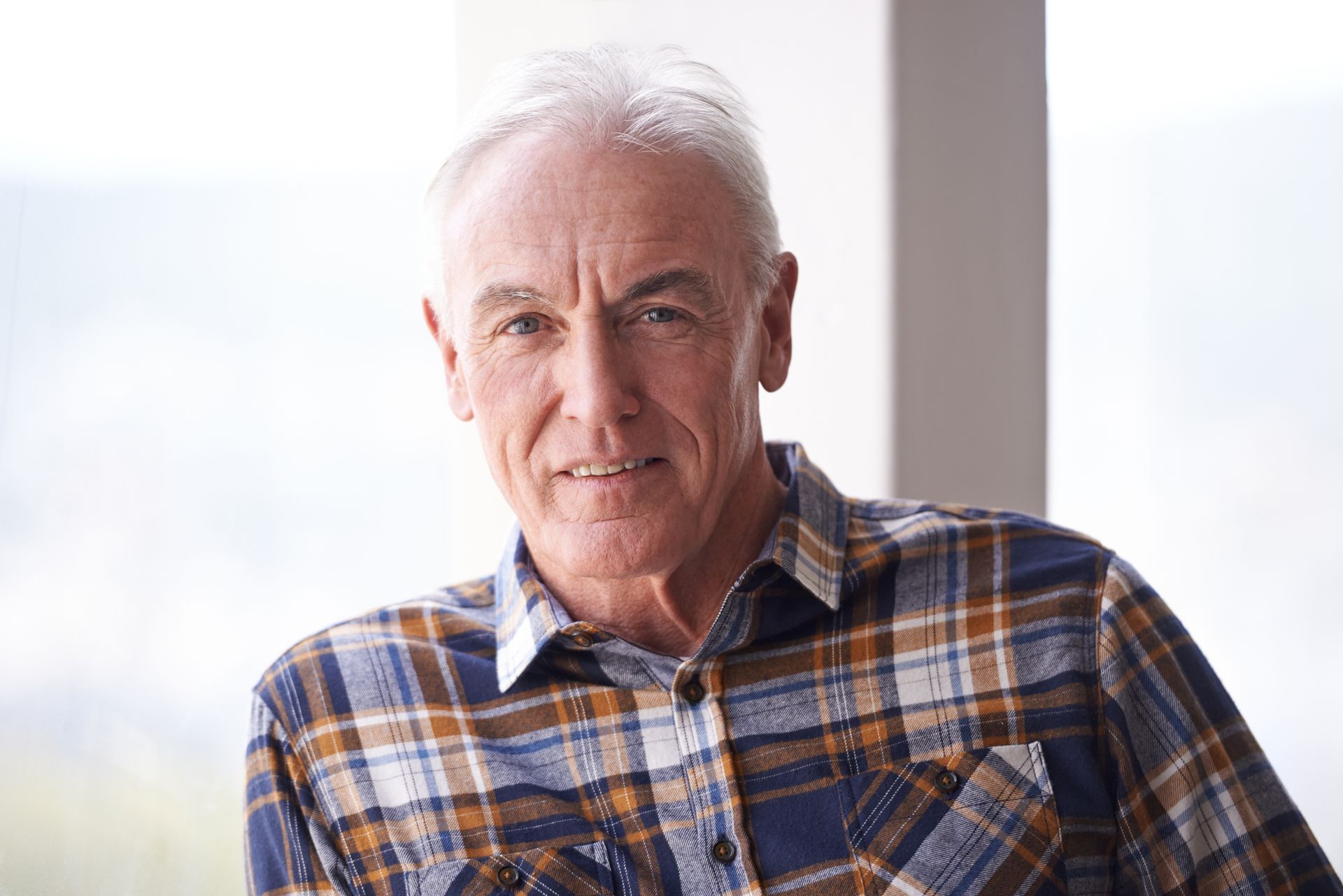 Man with gray hair, wearing a blue and brown plaid shirt, smiles at the camera.