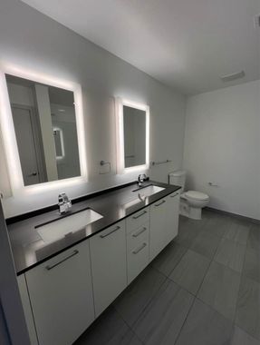 A bathroom with two sinks , two mirrors and a toilet.