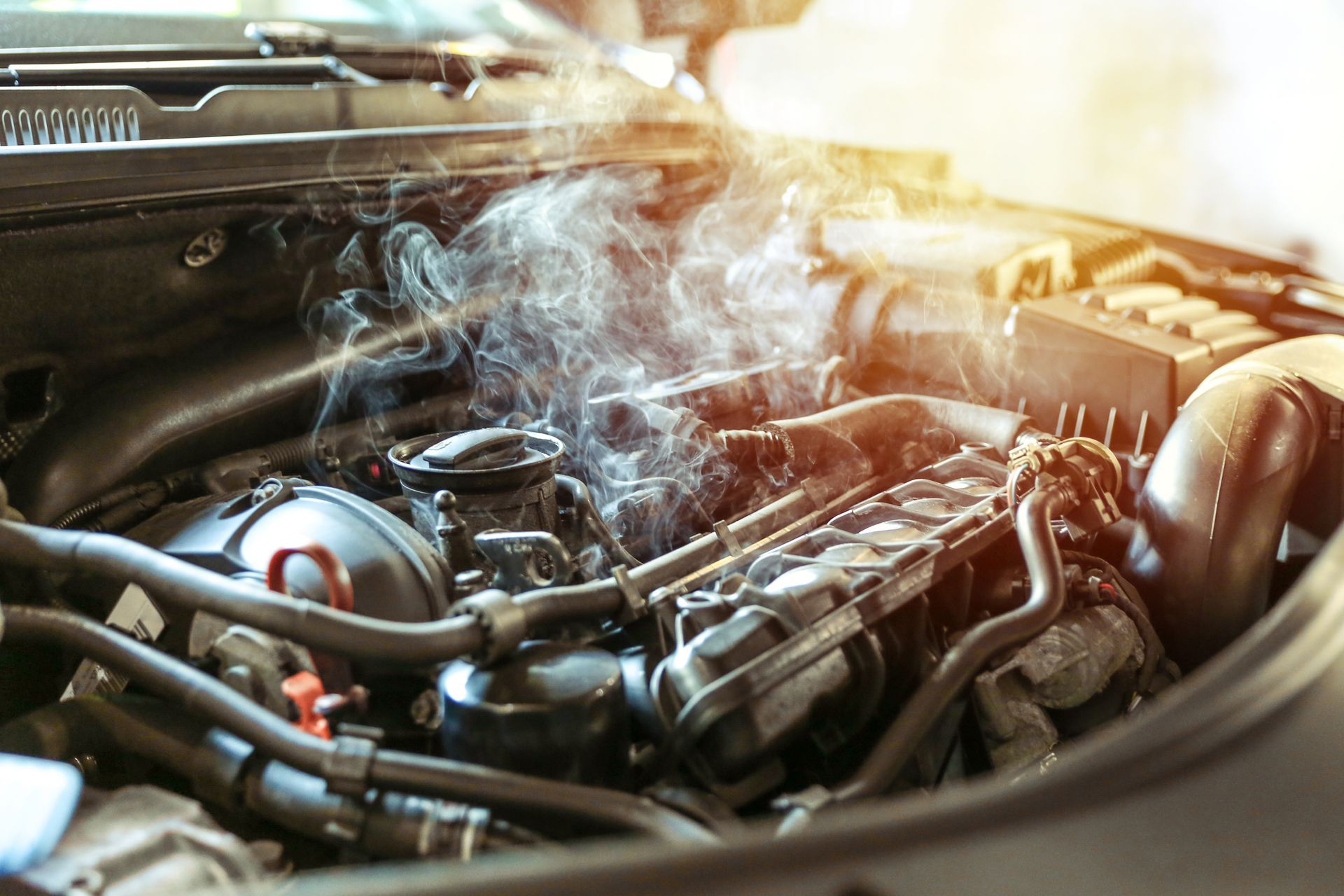 Thick smoke billows from the open hood of a car engine, indicating a vehicle breakdown or overheating.