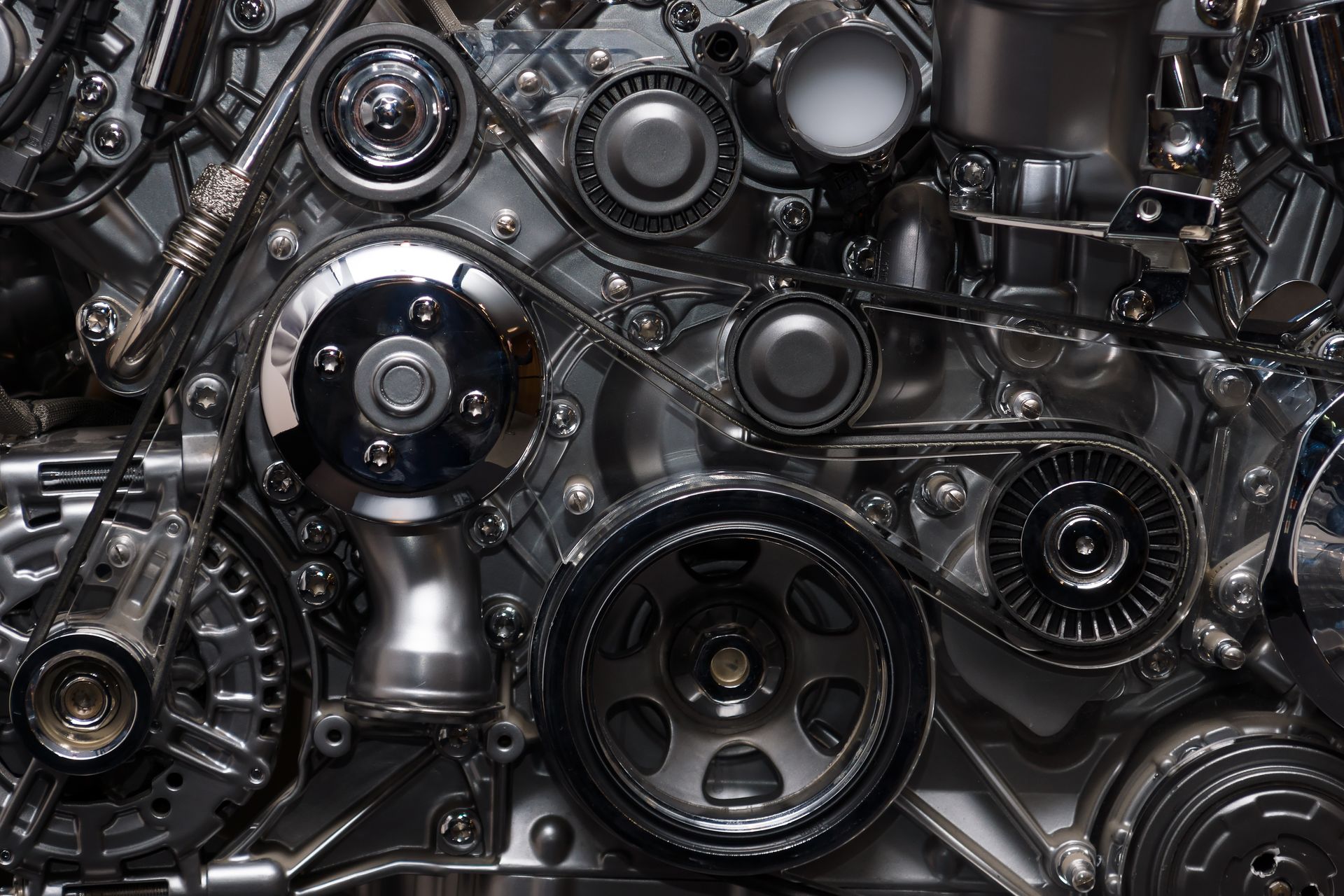 Close-up of a complex car engine, featuring metallic pulleys and belts interconnected in a mechanical assembly.