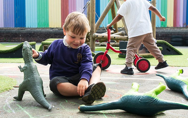 A young boy is sitting on the ground playing with toy dinosaurs.