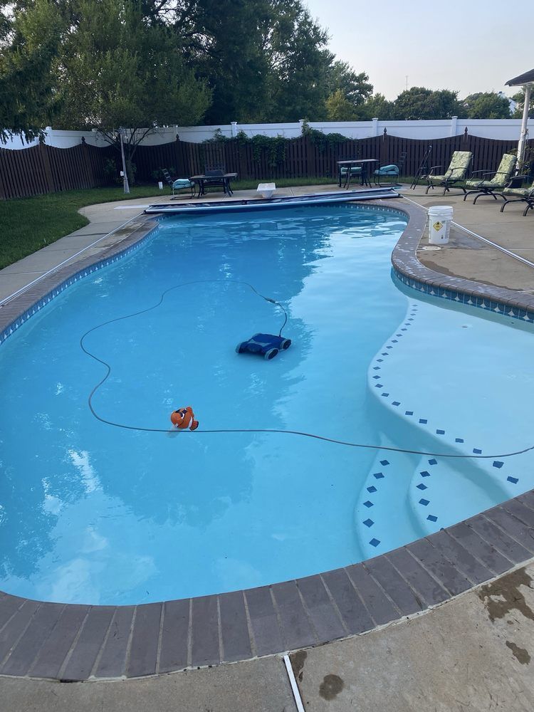 Backyard swimming pool with a pool vacuum floating in blue water and a deck chair nearby