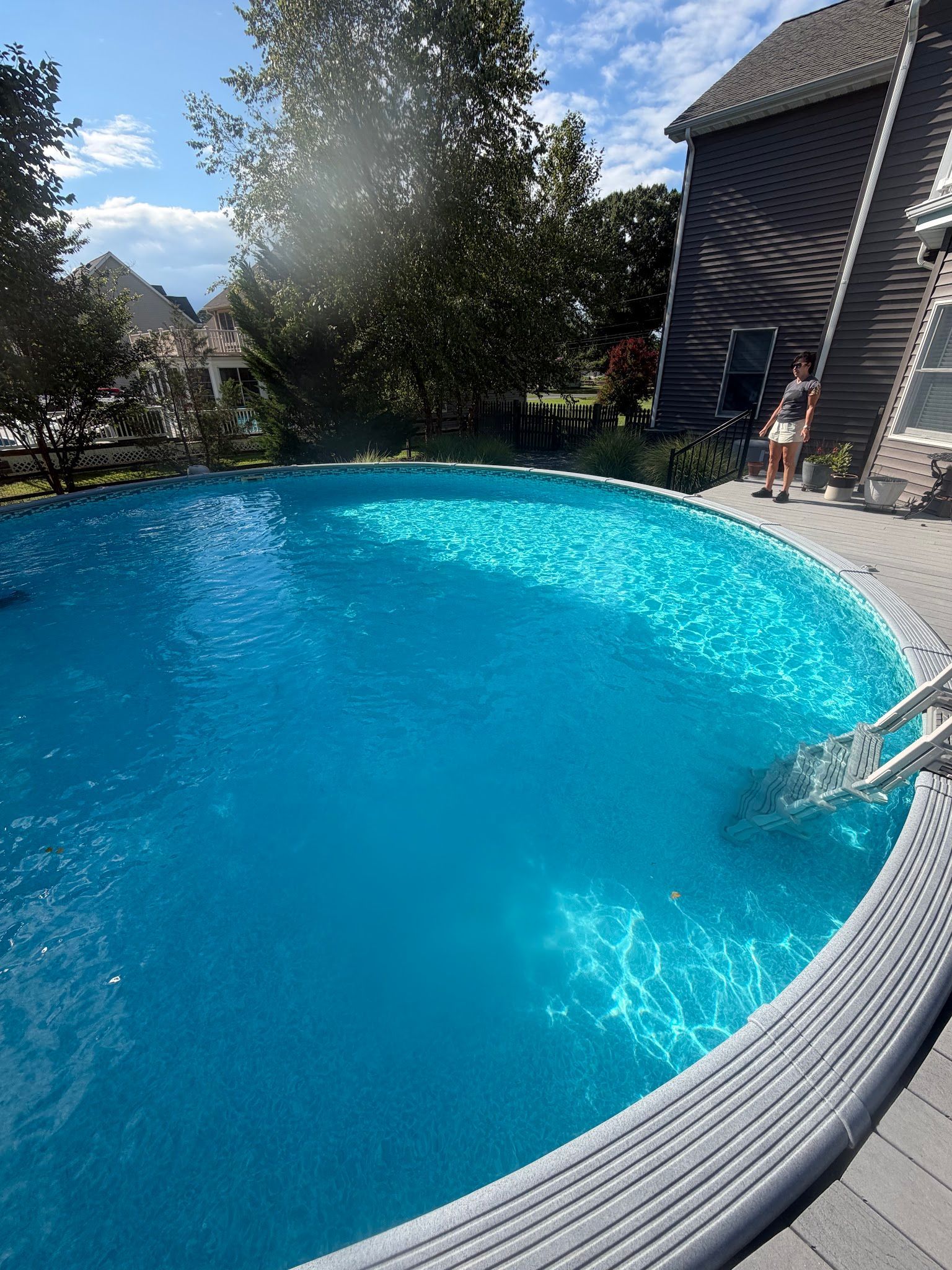 Backyard swimming pool with bright blue water beside a house on a sunny day