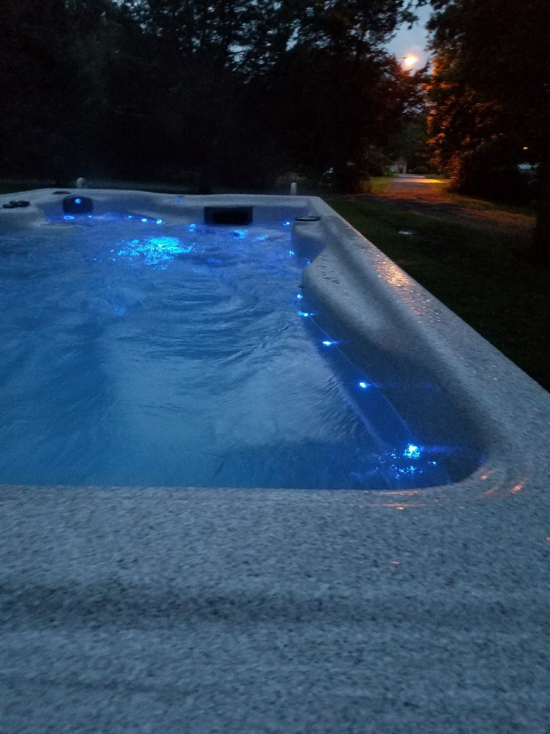 Illuminated backyard swimming pool at dusk with blue underwater lights and calm water