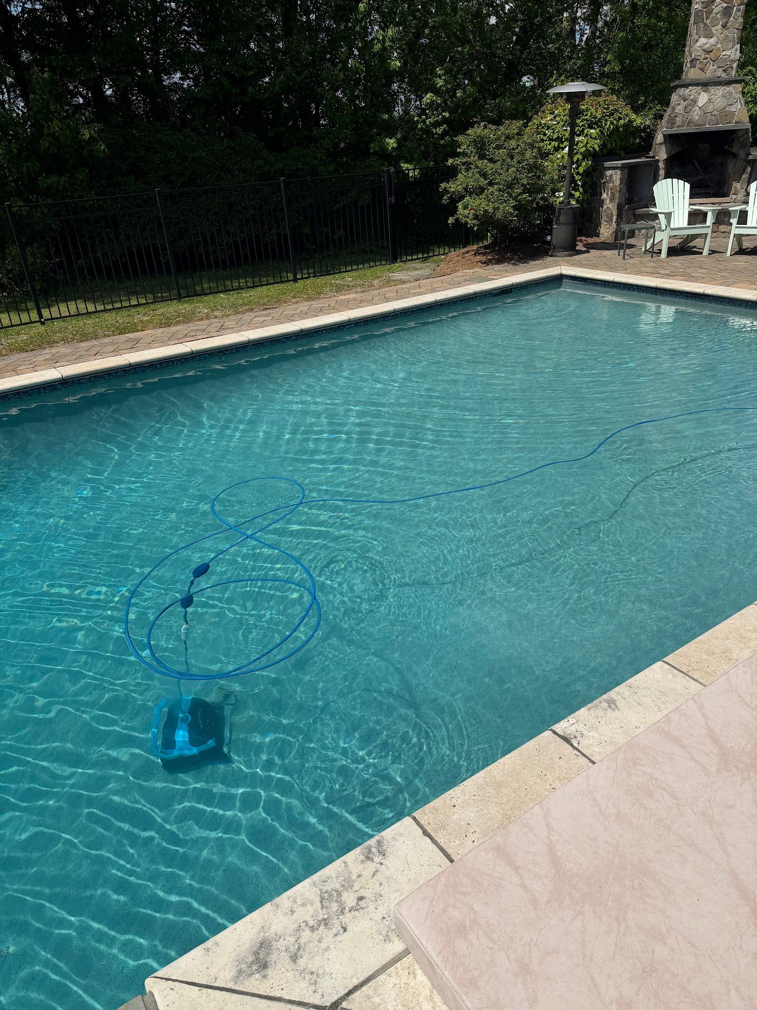 Backyard swimming pool with clear blue water and a vacuum cleaner floating near the center