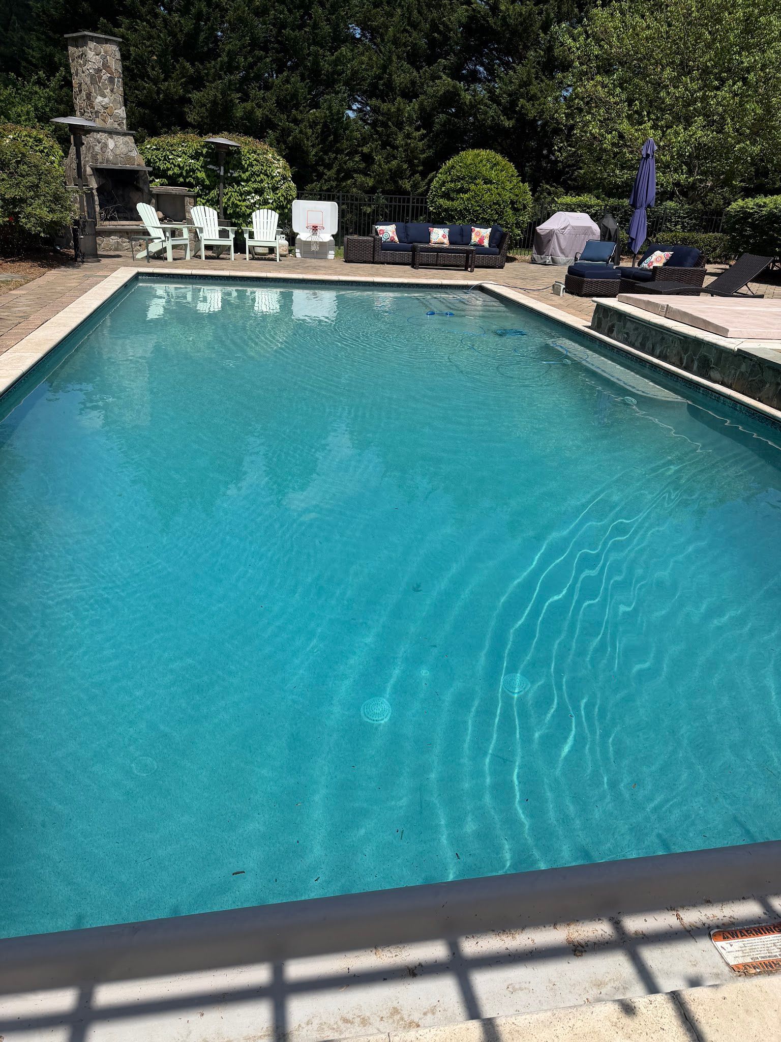 Backyard swimming pool with turquoise water, lounge chairs, and greenery around the deck