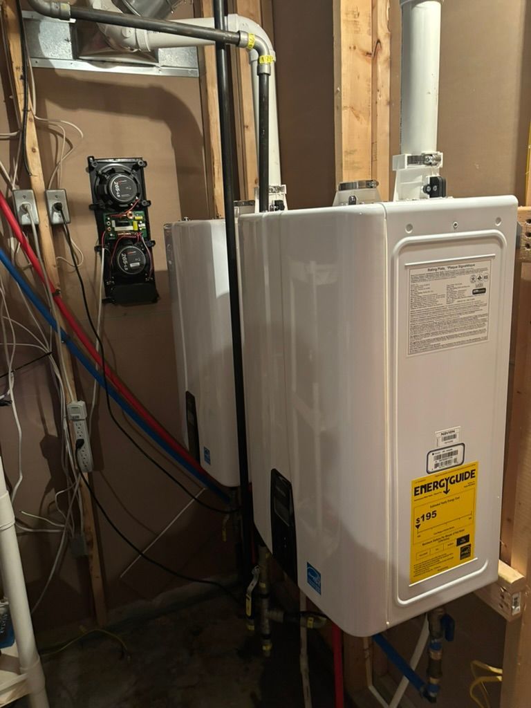 Wall-mounted white water heater in a utility closet with exposed pipes and wiring; breaker panel on left.