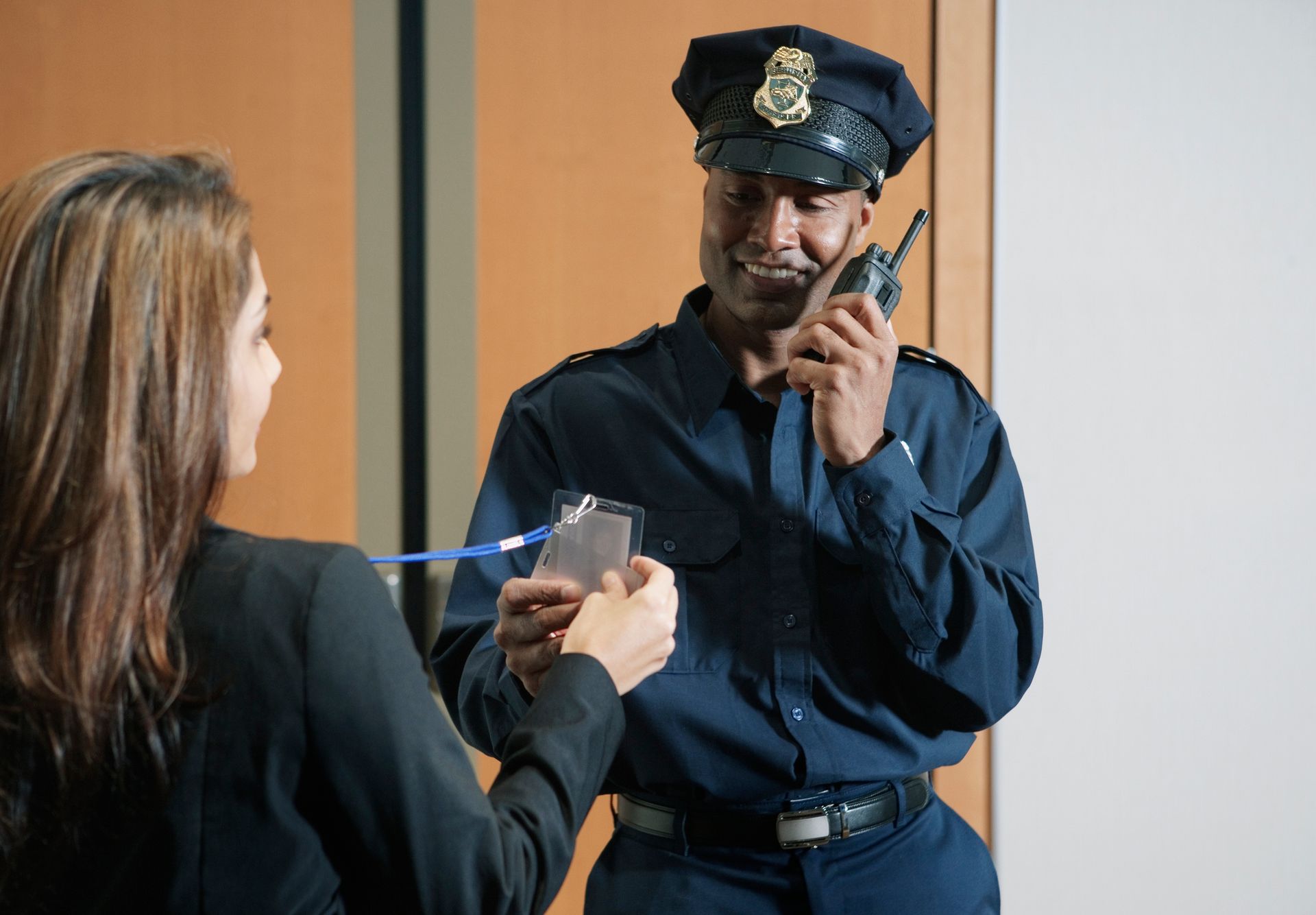 Security guard checking an ID badge. Guard in blue uniform smiles while holding a radio. Woman presents badge.