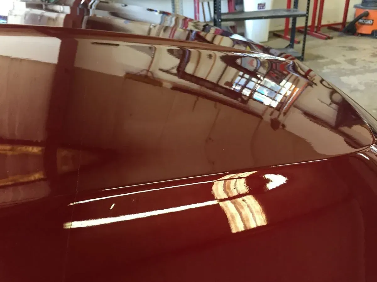 Glossy maroon car hood reflecting overhead lights in a garage