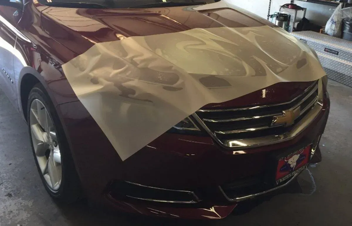 Maroon sedan with a protective sheet taped over the hood in a garage