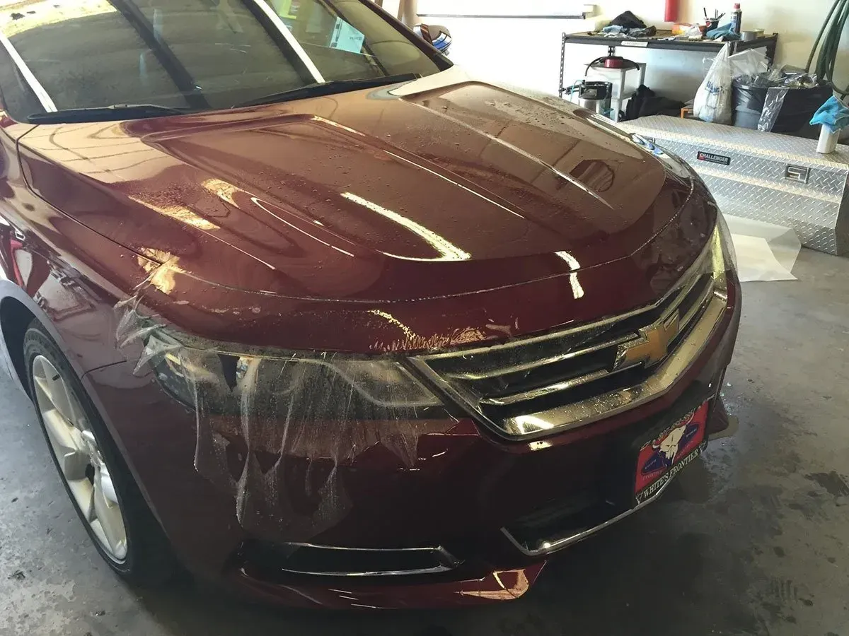 Maroon sedan in a garage with front-end damage and scratches on the hood and bumper