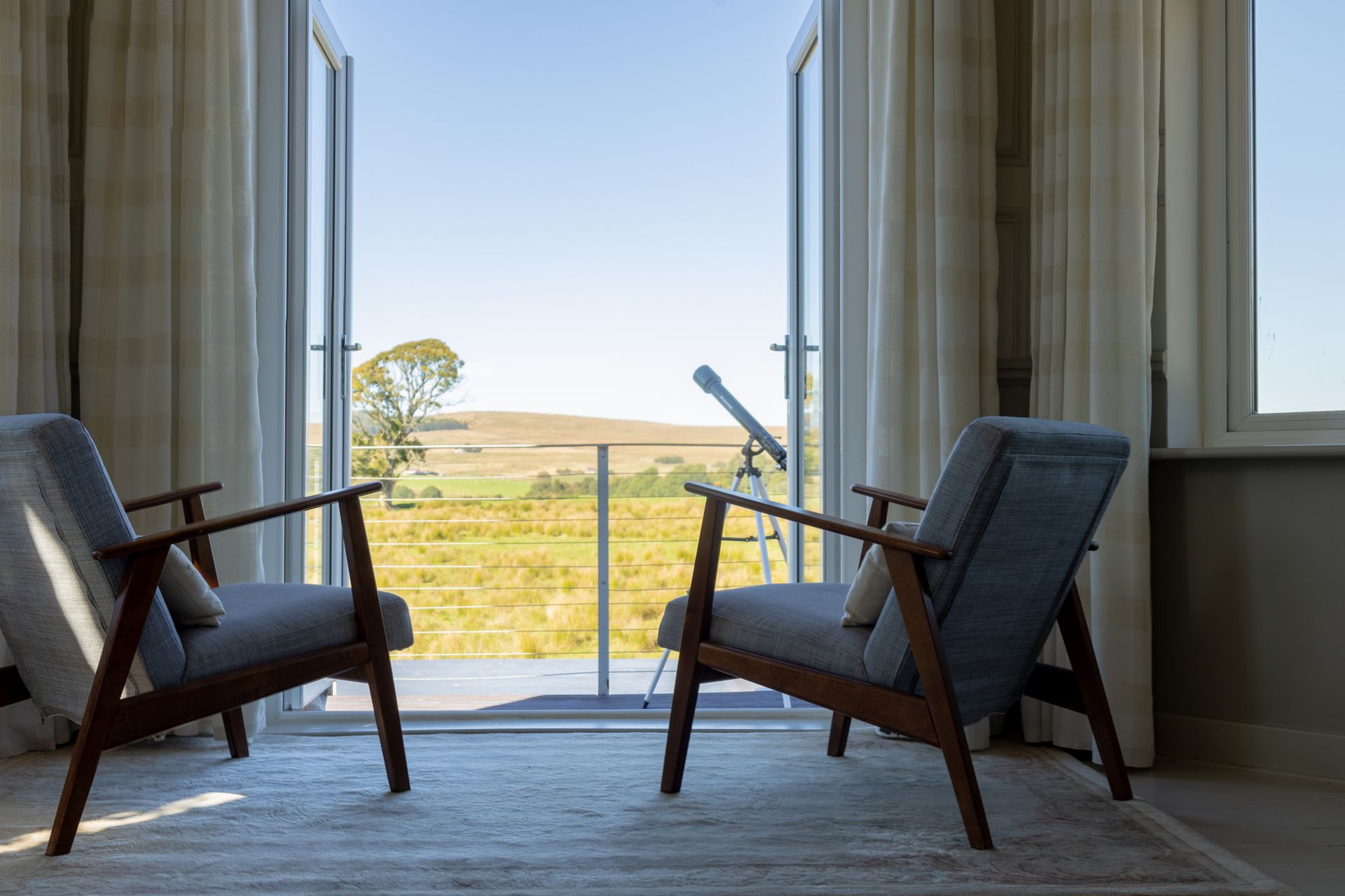 Two gray armchairs facing a sliding glass door with a view of fields and blue sky