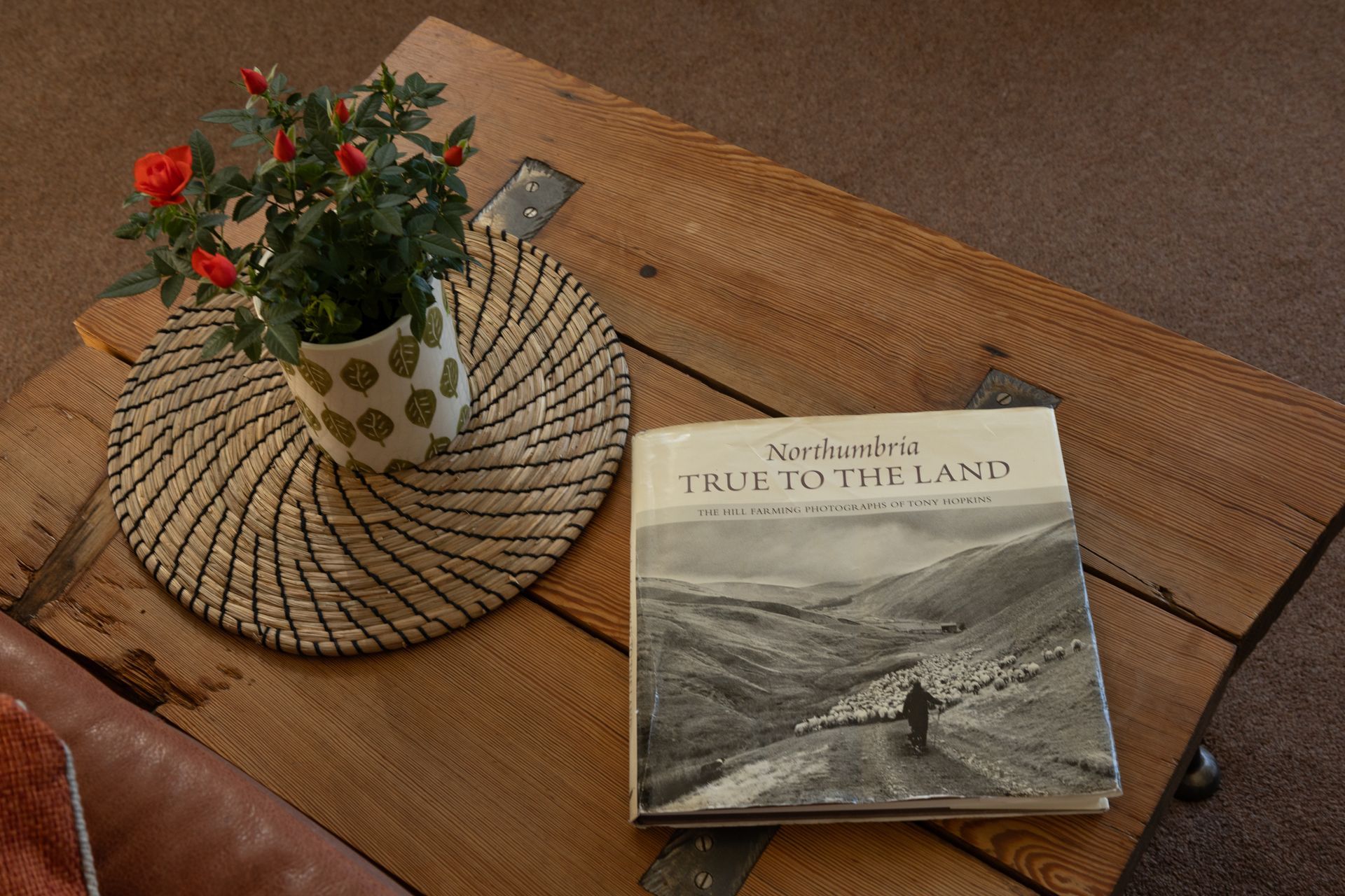 Book and potted flowers on a woven placemat atop a wooden table.