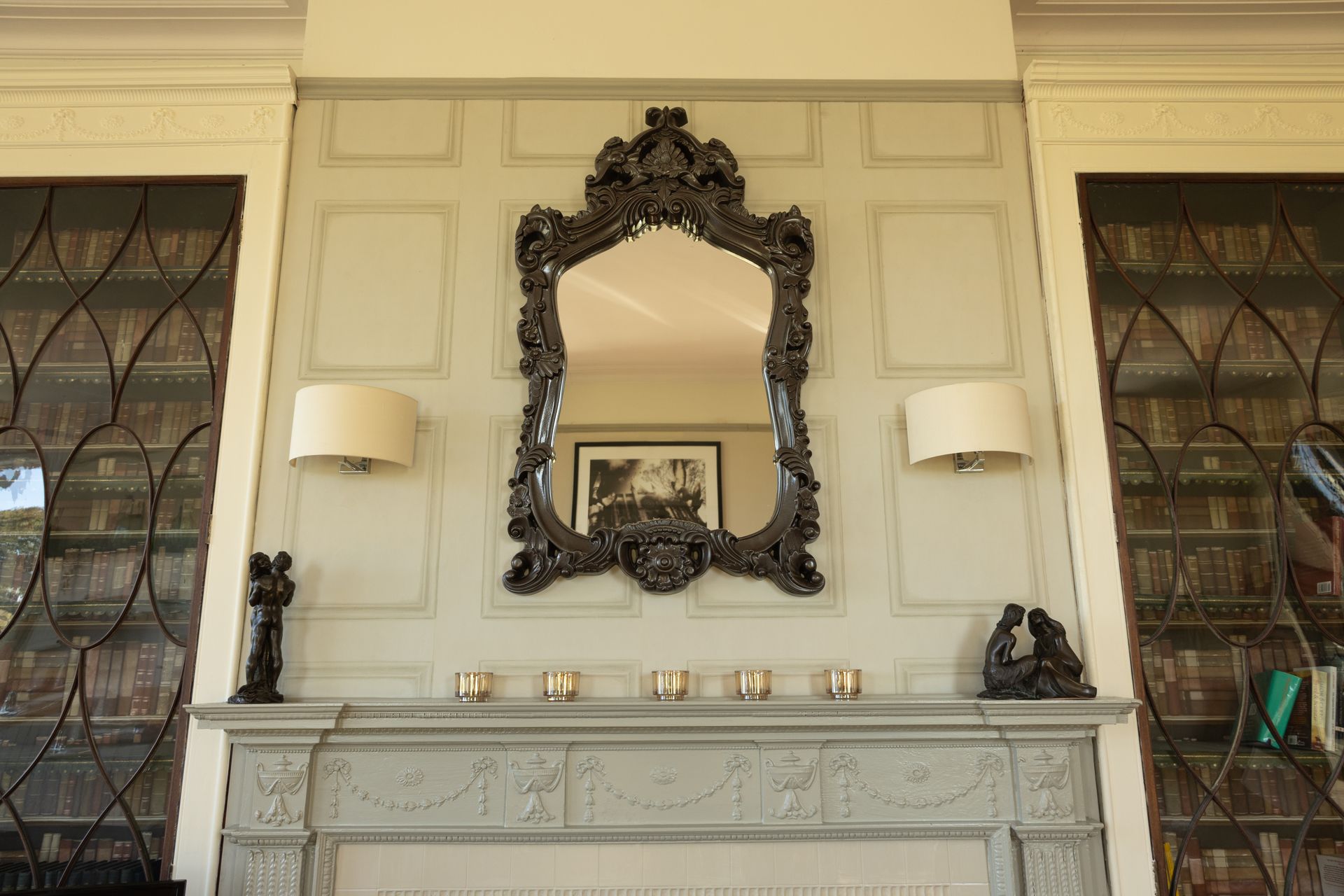 Ornate fireplace mantel with mirrored wall, sconces, and decorative items in a formal room