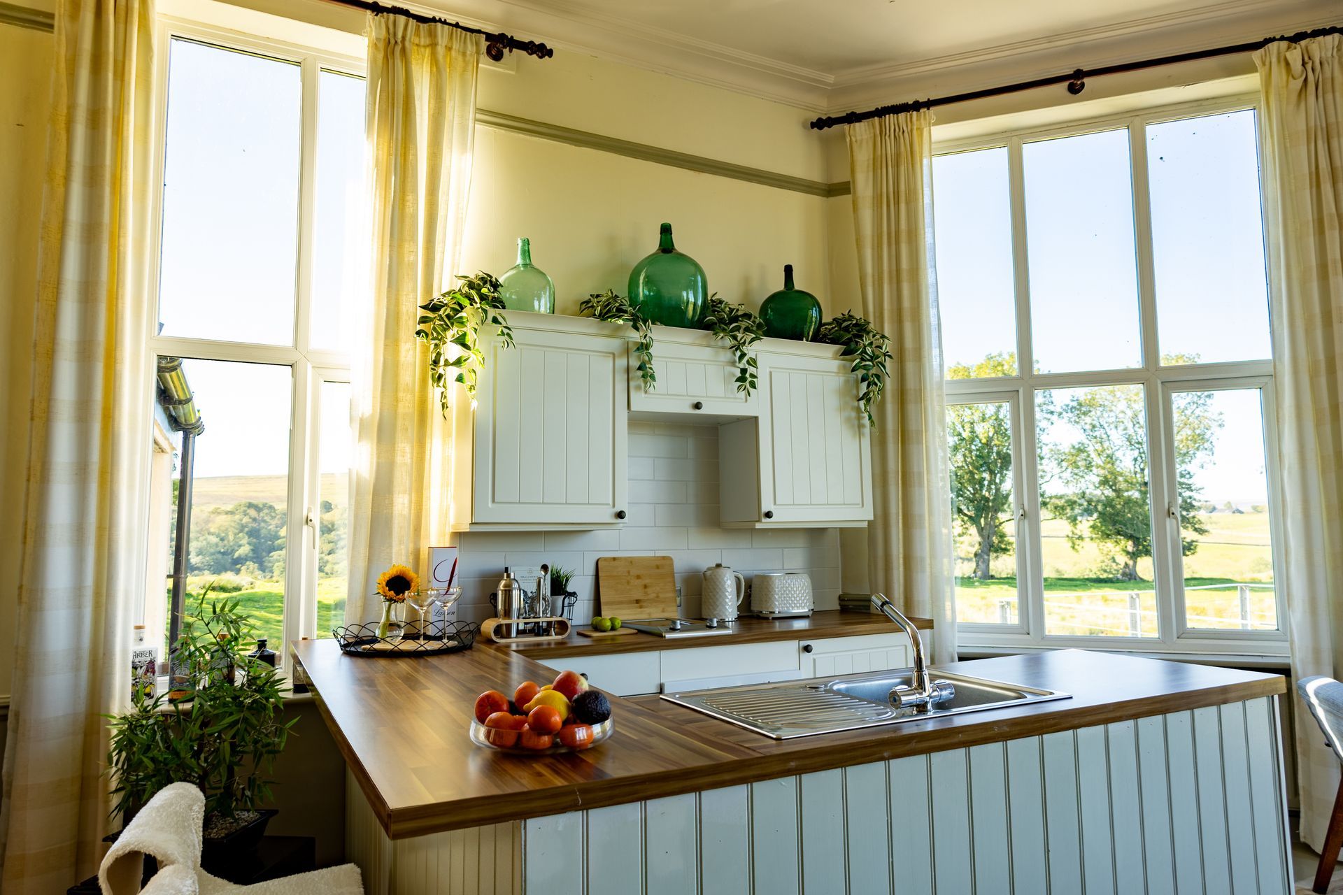 Bright kitchen with large windows, white cabinets, wooden island, and green glass decor.