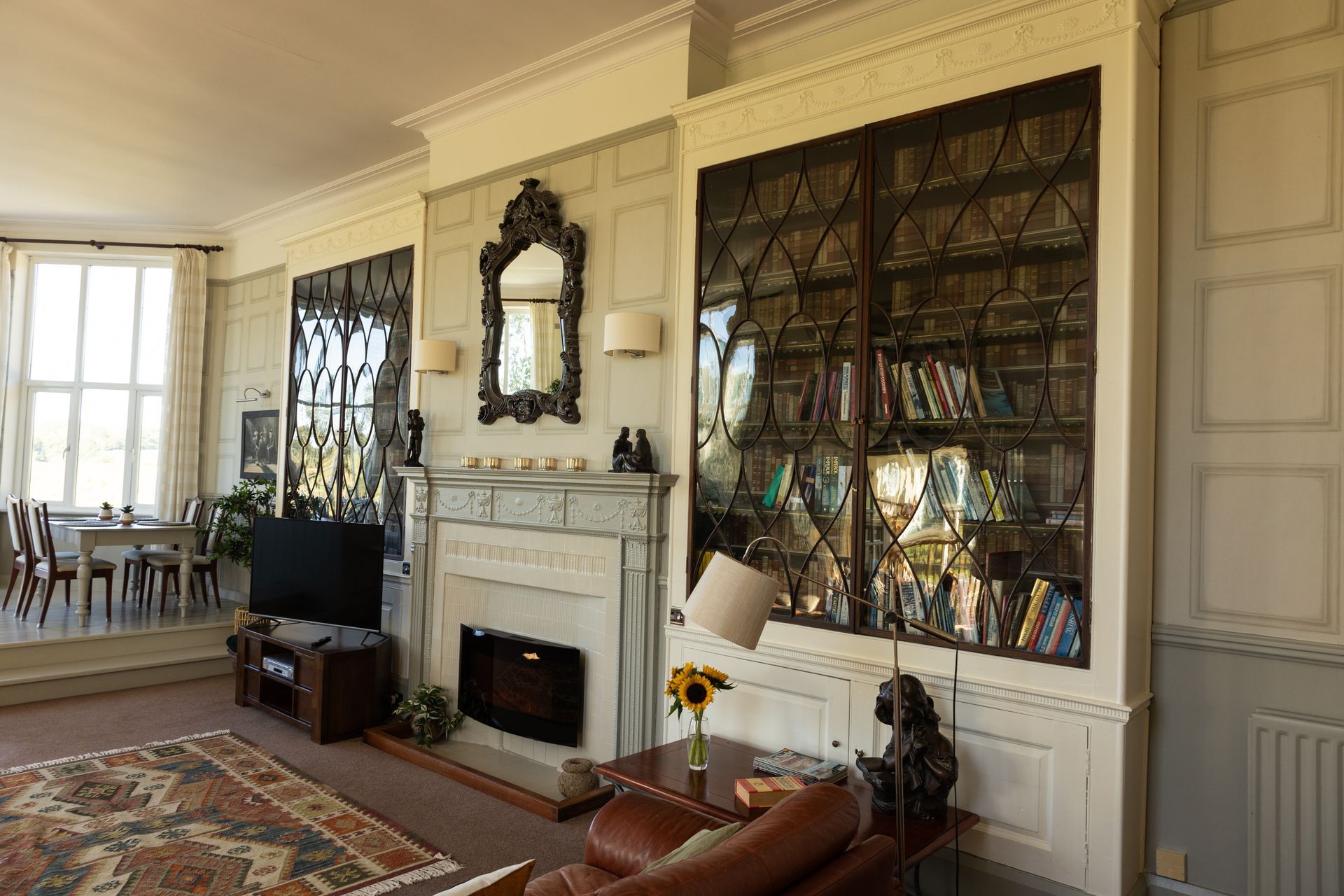Elegant living room with fireplace, tall windows, ornate mirror, and built-in bookshelves filled with books