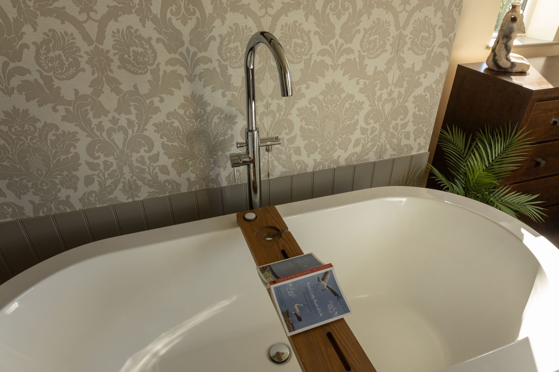Bathtub with a wooden board across it holding a book and a phone under a faucet