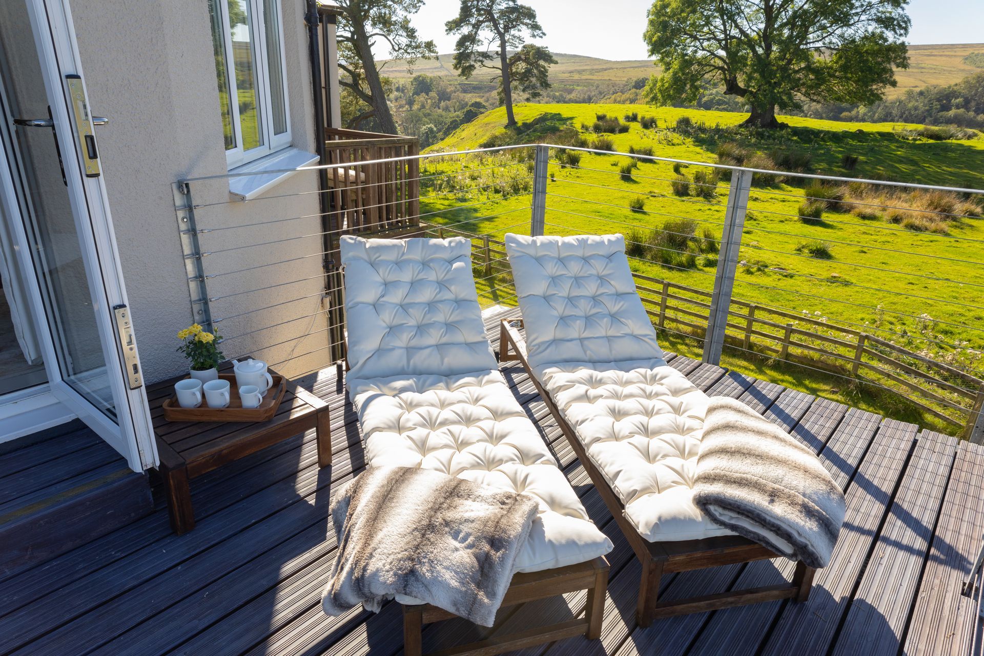 Two white lounge chairs on a deck overlooking a green countryside field